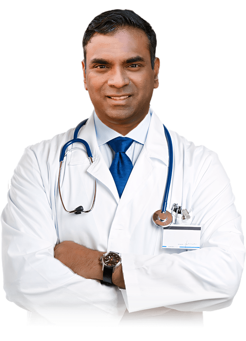 Dr. Pradeep Albert in a white lab coat and blue tie, stethoscope around his neck, arms crossed